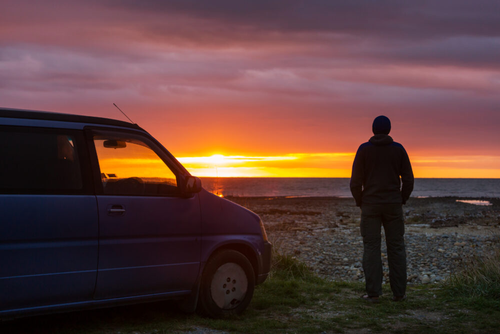 Sonnenuntergang vor dem ein Mensch steht. Daneben die Silhouette eines Wohnmobils