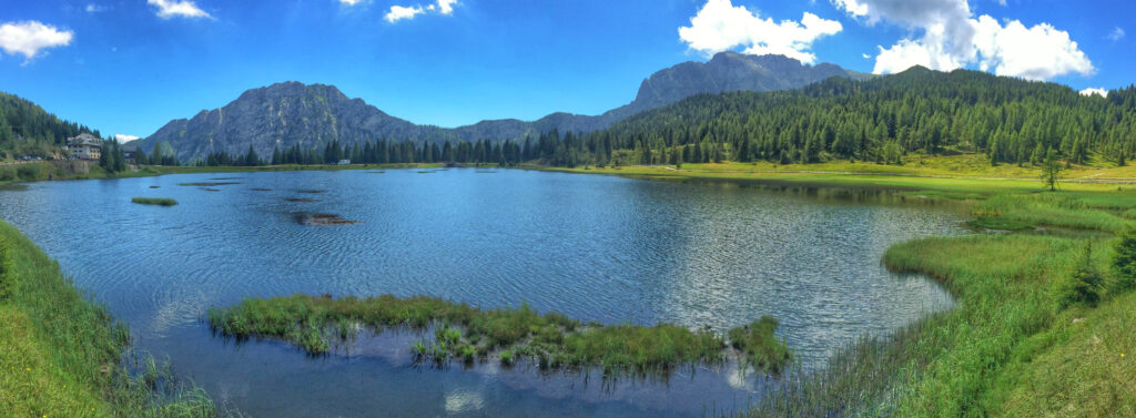 Panorama einer Bergrette. Davor ein Bergsee von Wäldern und Wiesen umgeben. 