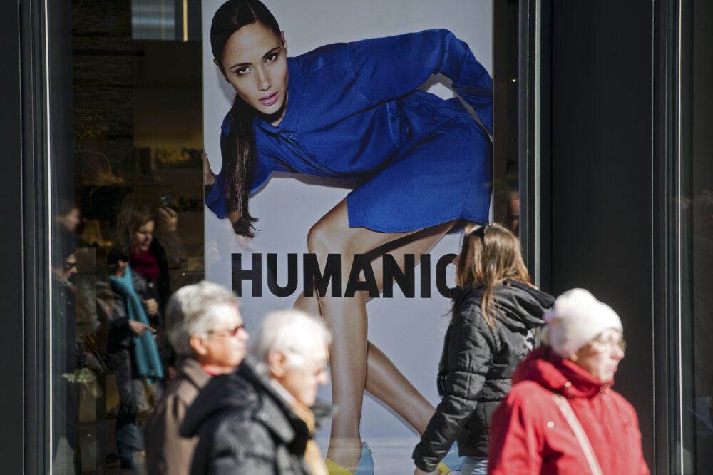 Ansicht eines HUMANIC-Plakates in einem Schaufenster. Menschen gehen daran vorbei.
