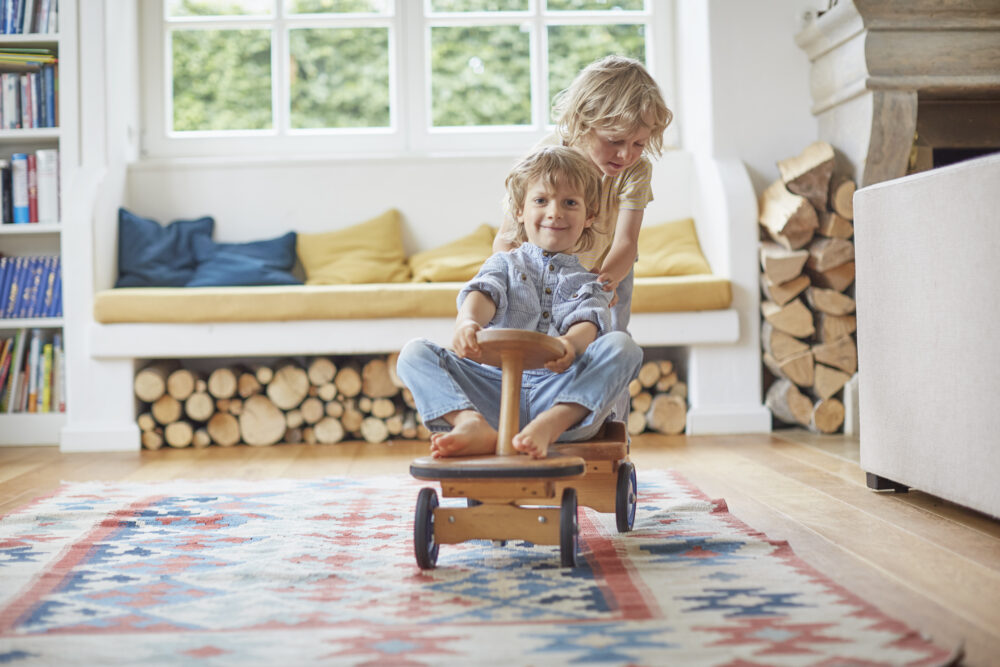 Zwei Kinder spielen mit einem Holzauto.