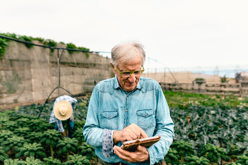 Bernard KRONE Älterer Herr mit einem Tablet in der Hand der auf in einen Anbaugebiet steht