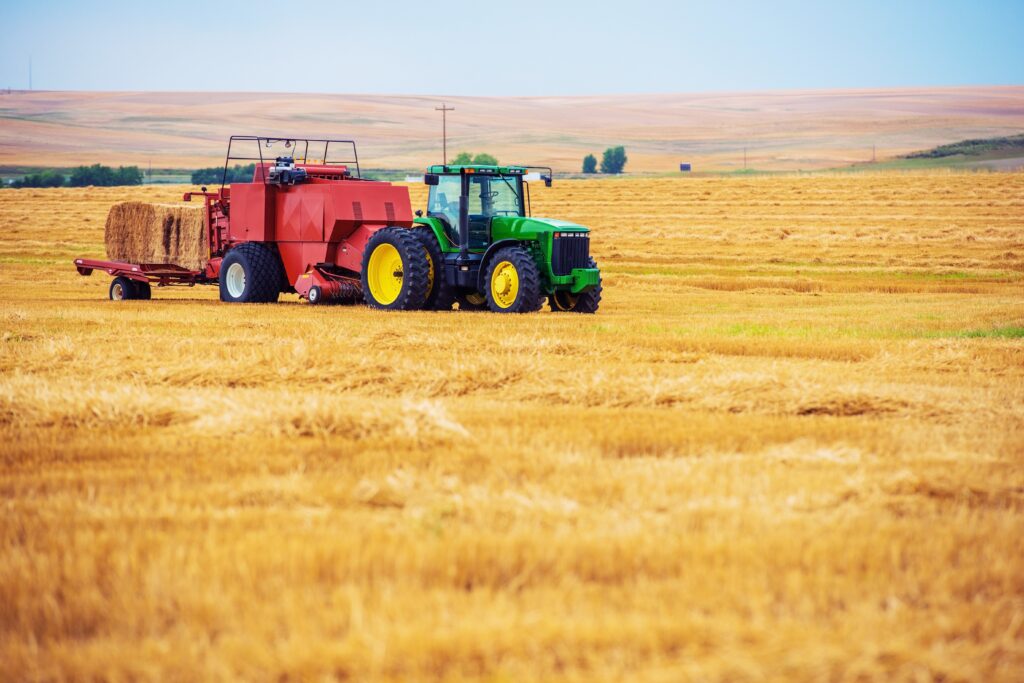 Bernard KRONE Riesiges Feld mit gelben Weizen und ein Traktor in grün mit gelben Reifen und einem roten Anhänger