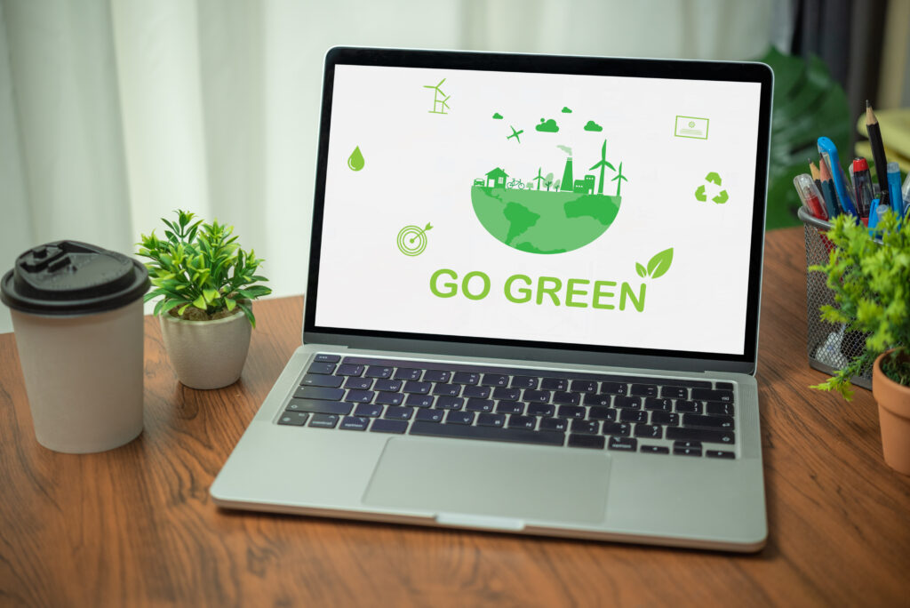 Holztisch mit einem Tablet auf dem GO GREEN steht und einige grüne Icons. rechts und links neben dem Tablet stehen ein Kaffeebecker, zwei Pflanzen und eine Dose mit Kugelschreibern