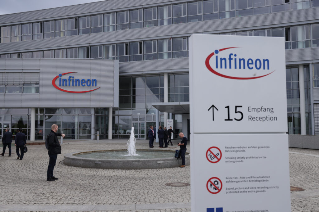 Firmengebäude von Infineon mit einem großen Logo über dem Eingang. Davor steht ein großes Schild mit infineon das auf 15 Empfang Reception verweist