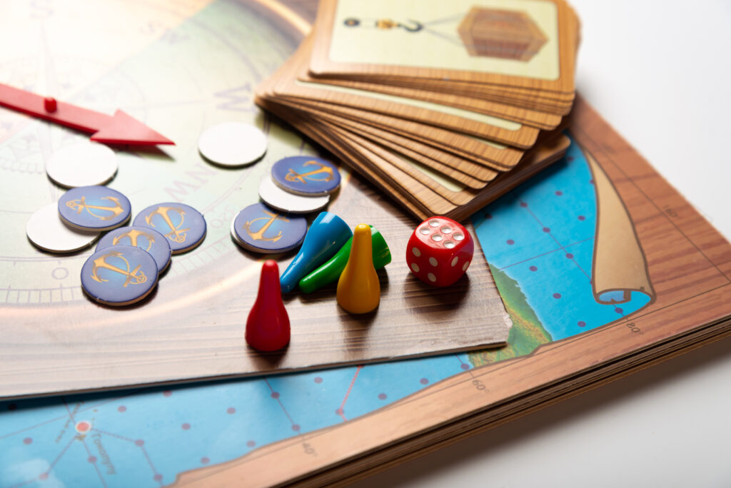 Spielbrett mit rotem Würfel, Figuren, Karten und einem roten Pfeil in Nahaufnahme