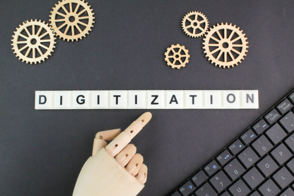 schwarzer Hintergrund, eine Computerhand die auf Digitization zeigt, eine Tastatur und Holzzahnräder