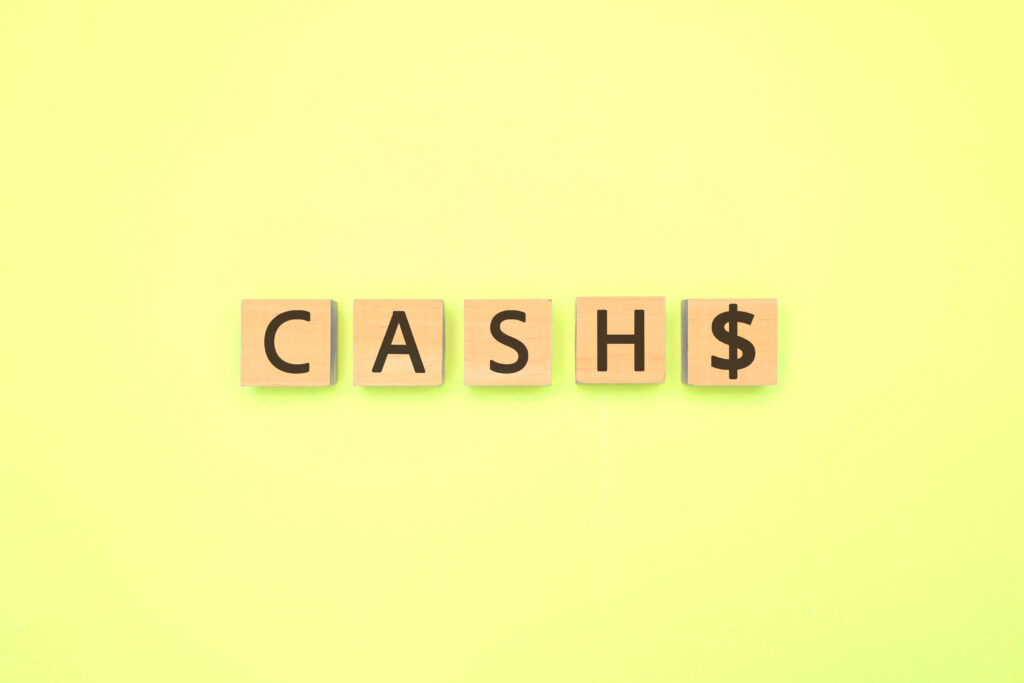gelber Hintergrund. Davor Cash$ geschrieben auf Holzbuchstaben