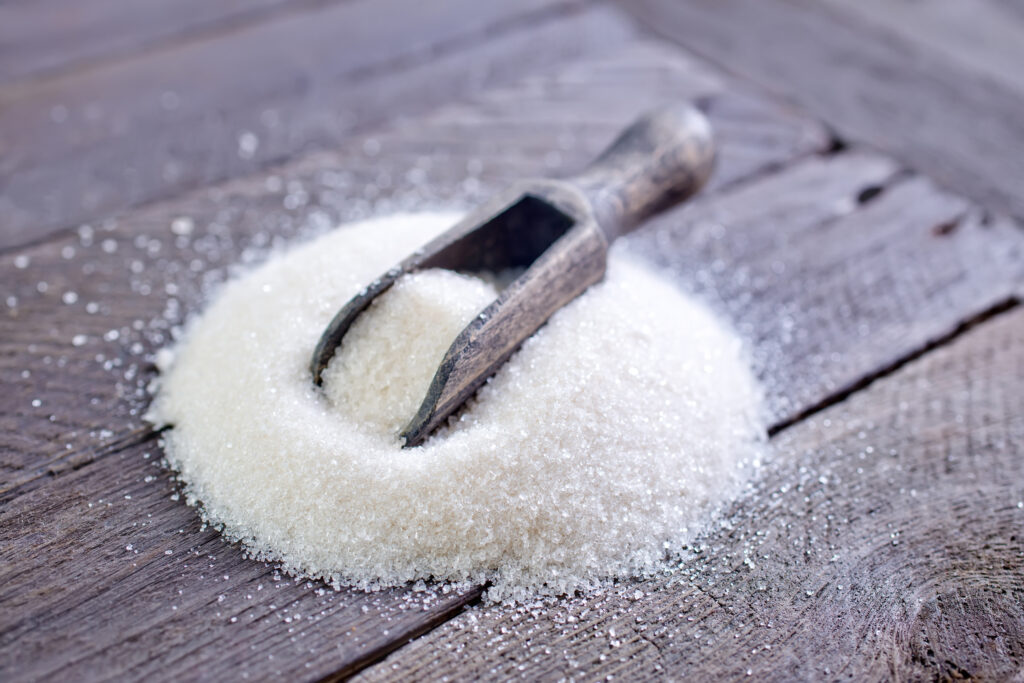 Zucker mit einer Zuckerschaufel auf einem Holzbrett