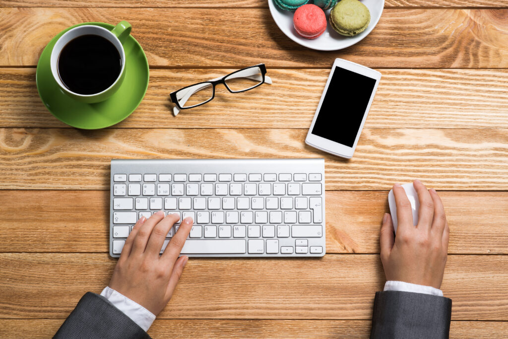 Holztisch mit einer Tastatur, Kaffeetasse, Brille, Handy, und zwei Händen